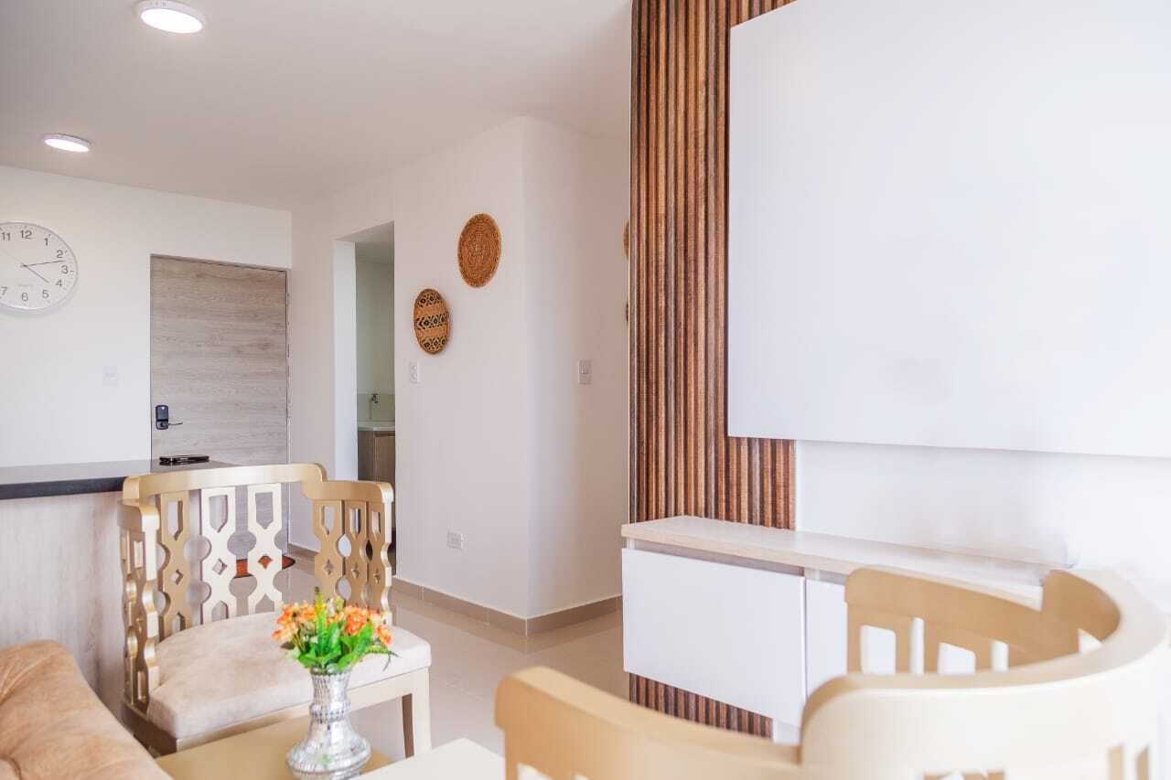 A modern living room with a sofa, a coffee table with a vase of flowers, a wooden chair, and a TV stand.