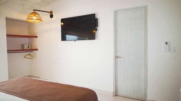 A bedroom with a bed, a television mounted on the wall, a door, and a hanging light fixture. - Cartagena Económica con Estilo y Comfot (Cartagena)