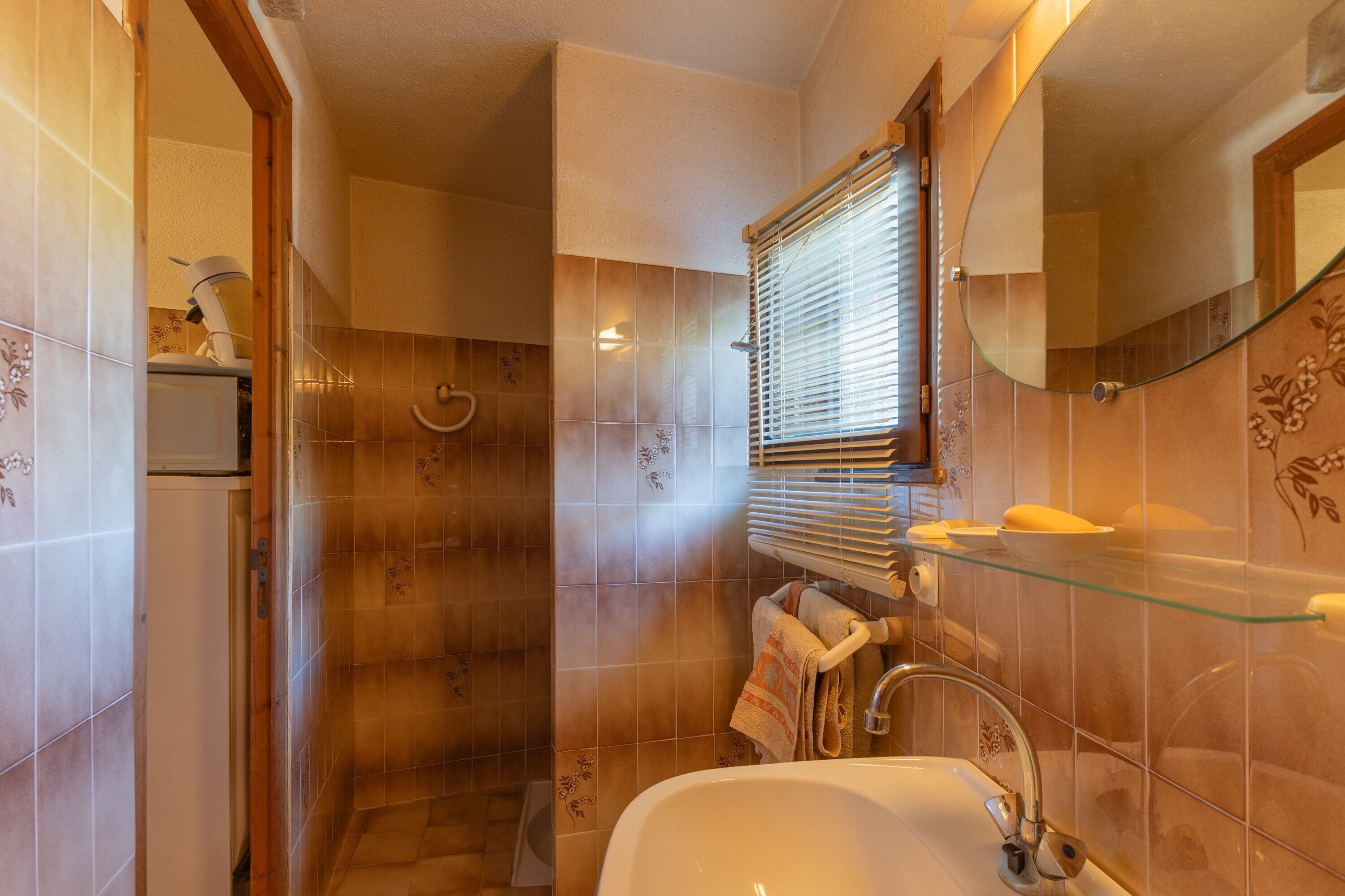 A bathroom with a glass shelf, a sink, a mirror, and a shower.