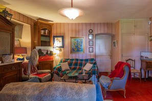 Ein gemütliches Wohnzimmer mit einem karierten Sofa, einem Holzschrank, einem Ventilator und einem Esstisch.