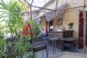 Ein Innenhof mit Metall-Pergola, Gartenmöbeln, Blumentöpfen und einem Gebäude mit Streifenmarkise.