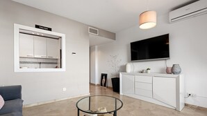 A modern living room with a glass coffee table, a sofa, a white cabinet, a mounted TV, and a ceiling fan. - Apartment 'Kym' with Mountain View, Wi-Fi and Air Conditioning (Duquesa)