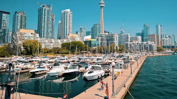 Un port de plaisance où de nombreux bateaux sont amarrés, une tour imposante en arrière-plan et une vue sur la ville avec ses gratte-ciel.