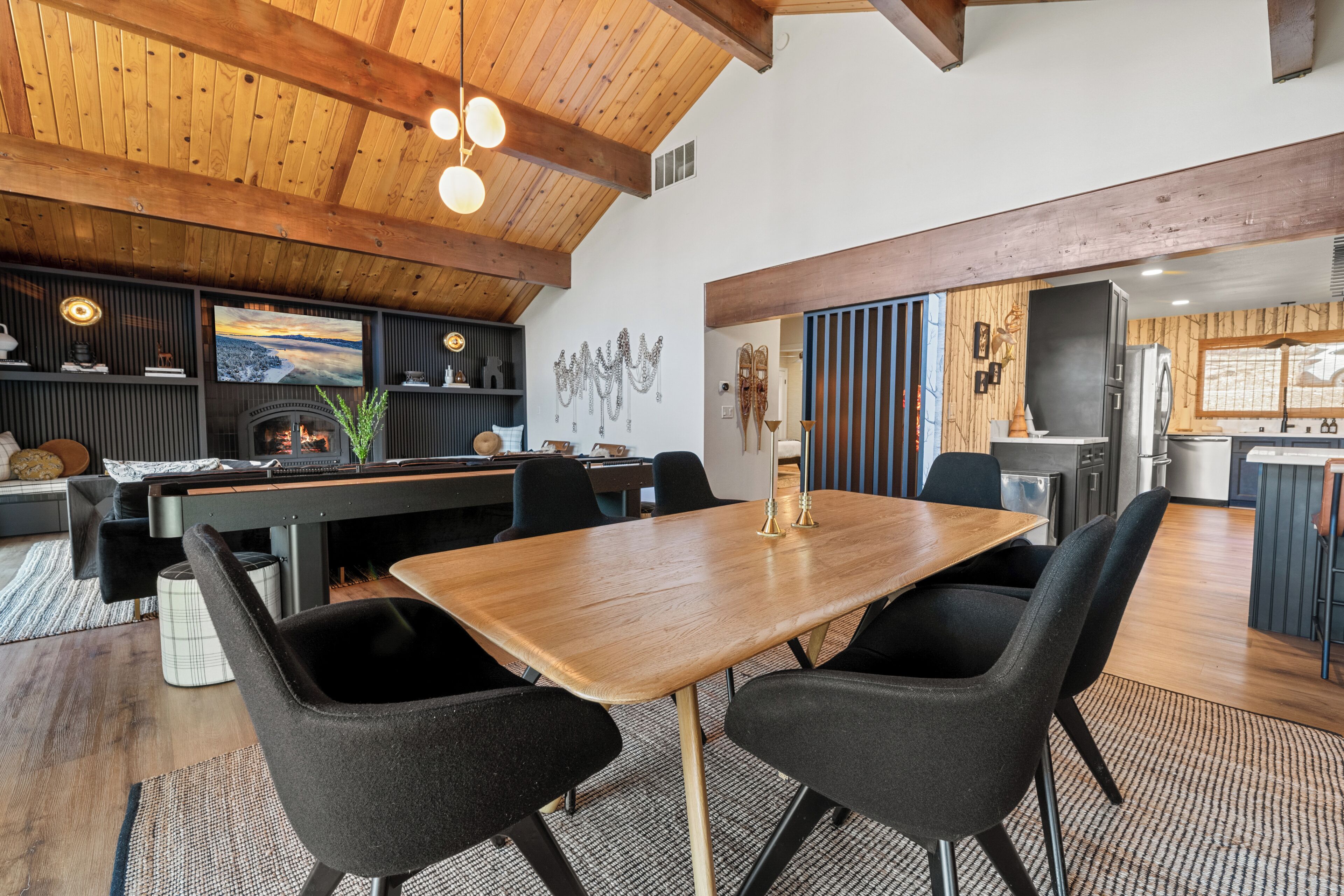 A spacious dining area with a wooden table and black chairs, a fireplace, and a kitchen area with modern appliances.