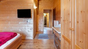 Ein Interieur einer Holzhütte mit einem Bett, einem Fernseher, einem Schminktisch und einer Tür zu einem weiteren Raum.