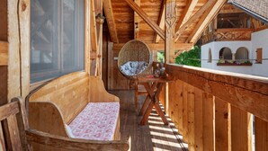 Ein hölzerner Balkon mit gepolstertem Sitz, einem Korbstuhl und einem Tisch mit einer Vase.