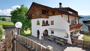 Ein traditionelles Chalet mit einer Steinterrasse, Holzbalkonen und Blick auf die umliegende Landschaft.