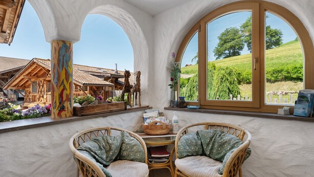 Ein Zimmer mit Blick auf einen Weinberg, ein Korbstuhl-Tisch mit Stühlen und ein Fenster mit Blick auf einen Baum.