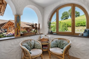 Une pièce avec vue sur un vignoble, une table en osier avec des chaises et une fenêtre donnant sur un arbre.