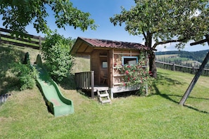 Une cabane en bois avec un petit porche, un toboggan vert et une jardinière.