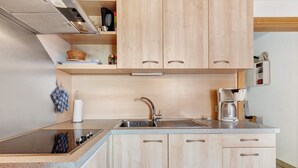 A modern kitchen with a built-in stove, stainless steel sink, wooden cabinets, and a coffee maker. - Apartment 'Kornblume' with Mountain View, Shared Garden and Wi-Fi (Meltina)