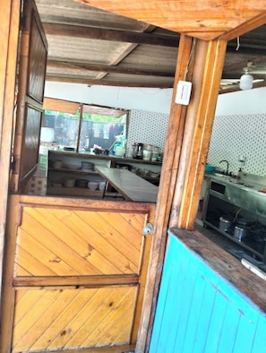 A rustic kitchen with wooden beams, a tiled backsplash, and a view of the outside.