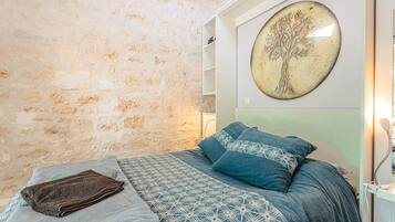 Ein Schlafzimmer mit Steinwand, einem Bett mit gemusterten Betttextilien, einer an der Wand befestigten Baumdarstellung und einer weißen Schrankwand.