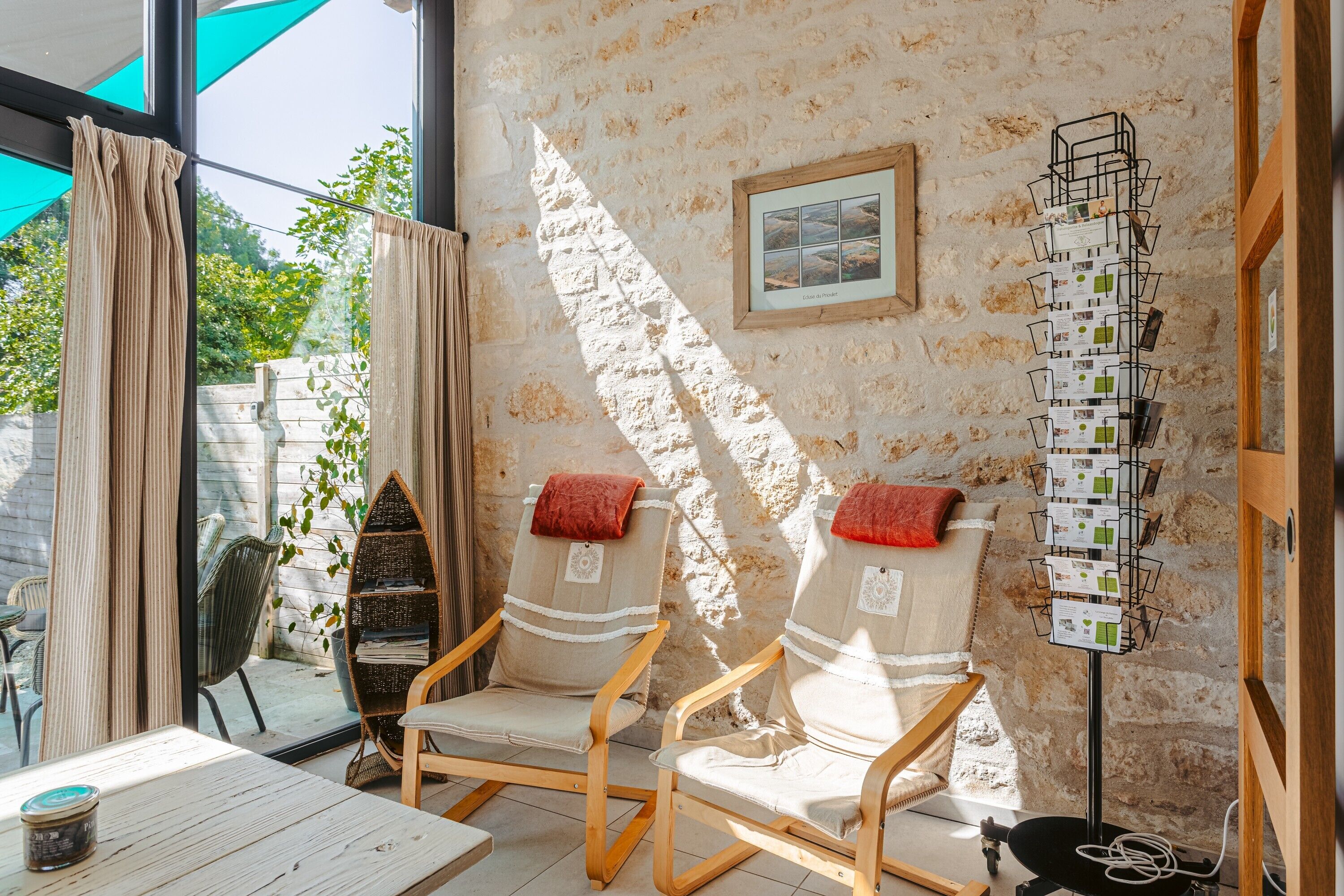 Une pièce comprenant deux chaises en bois, une table, un présentoir mural avec des cartes et un tableau encadré.