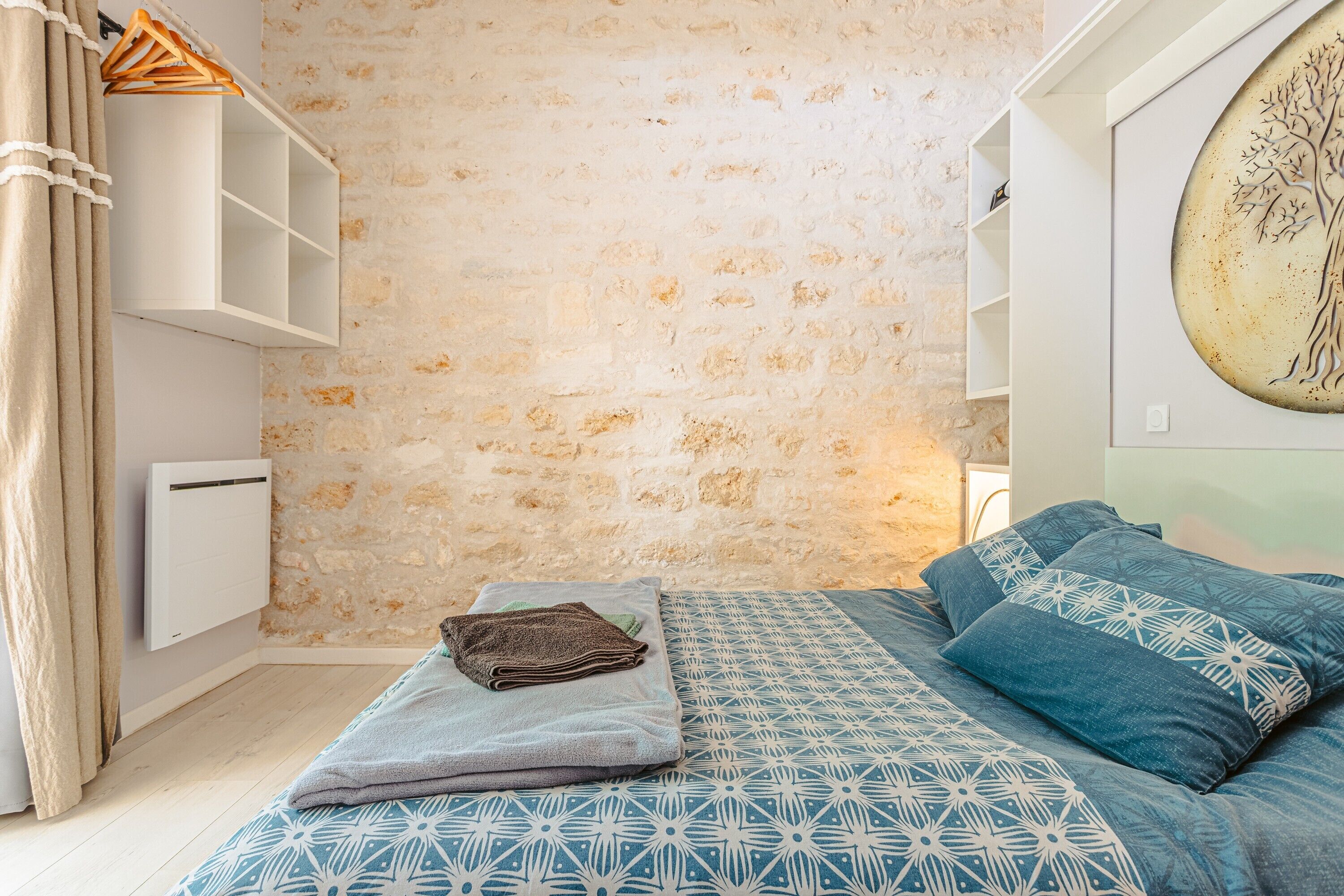 Een slaapkamer met een stenen muur, een bed met beddengoed met een patroon, een hangplank en een radiator aan de muur.