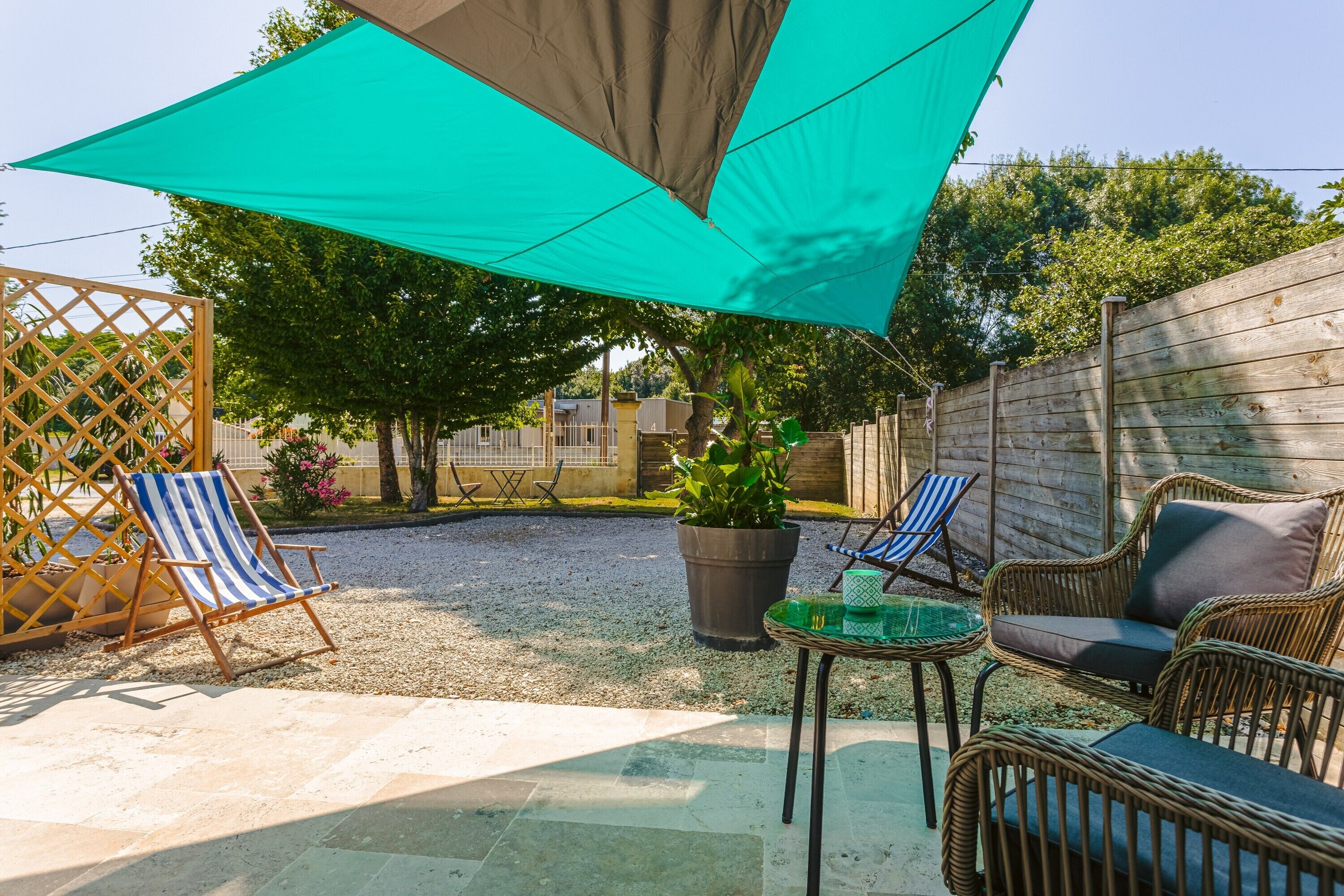 Un patio con una gran vela de sombra, mobiliario de mimbre y una planta en maceta.