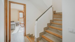 Un escalier avec des marches en bois et une rampe métallique, menant à une pièce dont le mur est blanc et qui possède une fenêtre.