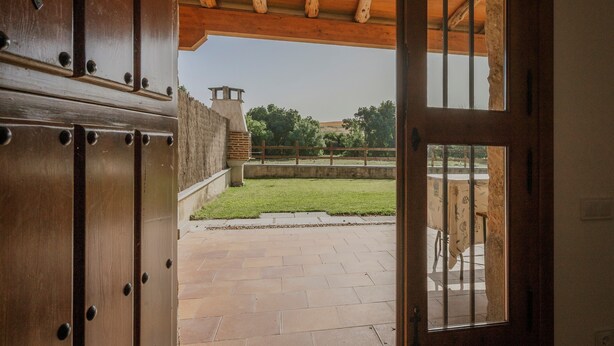 Une porte en bois ouverte donne sur un patio d’où l’on peut admirer une pelouse et un bâtiment situé au loin.