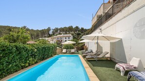 Ein Pool mit Liegestühlen und Sonnenschirmen, umgeben von Grünflächen und einem Gebäude.