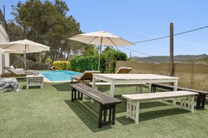 En udendørs terrasse med pool, liggestole og parasoller.