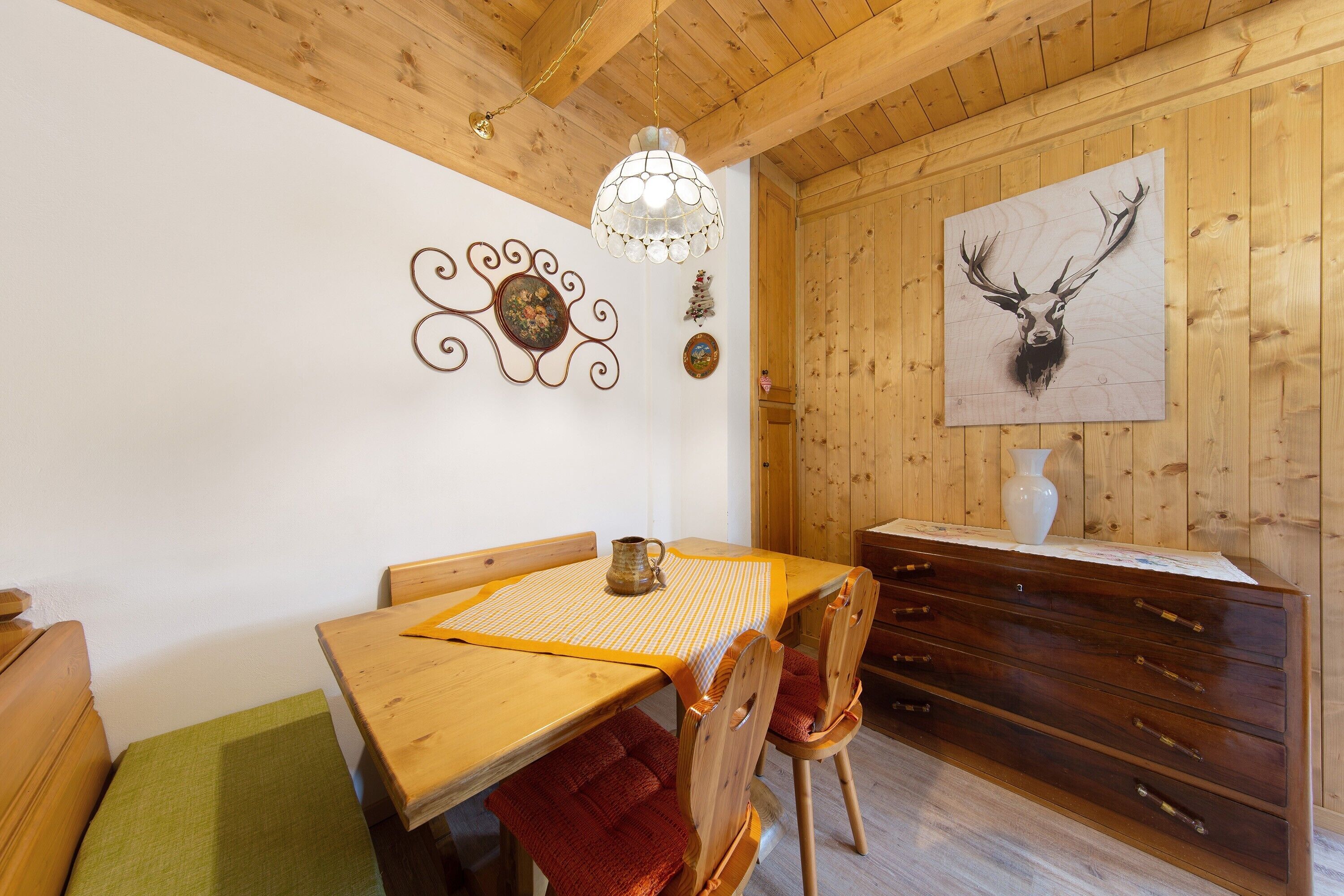 A wooden interior with a dining table, chairs, a chandelier, a cabinet, and wall decorations.