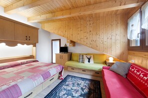 A wooden-paneled room with a bed, a sofa, a small table, and a television.