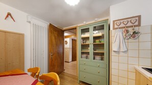 A room with a dining table, chairs, a cabinet, and a kitchen area with a tiled backsplash.