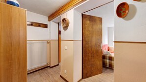 A hallway with wooden flooring, a radiator, a door, and a bed with a checkered blanket.