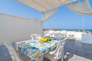 An outdoor dining area with a table set for two, white chairs, a tablecloth, and a view of the sea. - Apartment 'Donna Di Denari' with Sea View, Wi-Fi and Air Conditioning (Noto Marina)