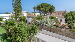 A residential area with houses, a large tree, and a fenced garden. - Apartment 'Donna Di Denari' with Sea View, Wi-Fi and Air Conditioning (Noto Marina)