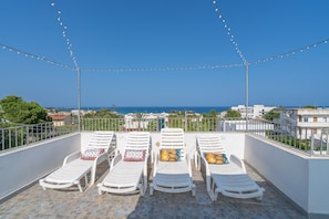 Una terraza en la azotea con cuatro sillones blancos, luces de cuerda y vista al mar.