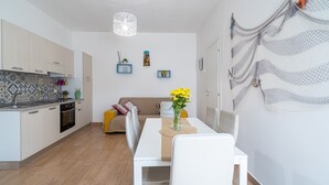 A modern kitchen with white cabinets, a dining table with chairs, a vase with flowers, and a decorative wall hanging. - Apartment 'Donna Di Denari' with Sea View, Wi-Fi and Air Conditioning (Noto Marina)