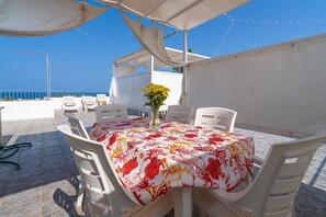 Un espace extérieur abrité, aménagé avec une table pour deux, des chaises et un vase rempli de fleurs jaunes.