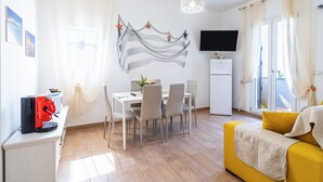 A modern living room with a dining area, a sofa, a flat-screen TV, and a refrigerator. - Apartment 'Re Di Denari' with Sea View, Wi-Fi and Air Conditioning (Noto Marina)