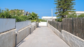 A narrow, paved pathway flanked by concrete walls and a wooden fence, leading to a building with a white facade. - Apartment 'Re Di Denari' with Sea View, Wi-Fi and Air Conditioning (Noto Marina)