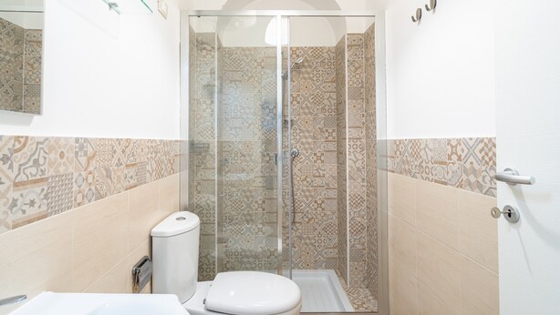 A bathroom with a toilet, sink, and shower with patterned tiles.