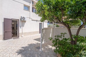 A building with a tiled patio, a tree, and a door with a shutter.