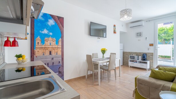 A modern kitchen with a sink, a dining area with a table and chairs, a TV mounted on the wall, and a sofa in the living area. - Apartment 'Almàsalo Re Di Coppe' with Private Terrace, Wi-Fi and Air Conditioning (Noto Marina)