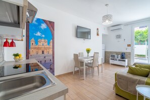 A modern kitchen with a sink, a dining area with a table and chairs, a TV mounted on the wall, and a sofa in the living area. - Apartment 'Almàsalo Re Di Coppe' with Private Terrace, Wi-Fi and Air Conditioning (Noto Marina)