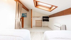 Ein Schlafzimmer mit zwei Betten, einem Oberlicht, einer Heizung und einer Holzbalkendecke.
