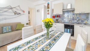 Eine moderne Küche mit gefliestem Spritzschutz, ein Essbereich mit einem gemusterten Tischlein und eine Wohnbereich mit einer Couch und dekorativen Kissen.