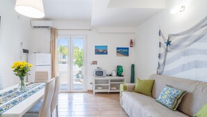 Ein Wohnzimmer mit einer Couch, einem Esstisch mit Stühlen, einem Fernseher und einer Küchenzeile mit einer Mikrowelle.