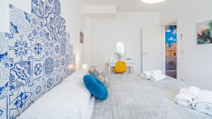 Ein Hotelzimmer mit Bett, Schreibtisch, Stuhl, Spiegel und Blick auf ein Gebäude durch eine geöffnete Tür.