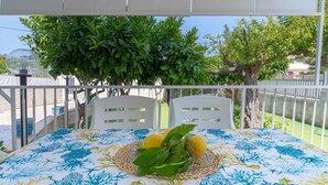 Ein Balkon mit Tisch für zwei Personen, einem weißen Geländer und Blick auf einen Baum sowie ein Gebäude im Hintergrund.