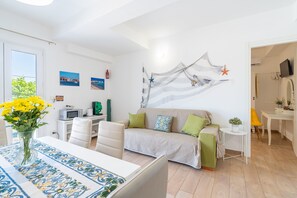 A modern living room with a sofa, a dining table with a patterned table runner, a TV, and artwork on the walls.