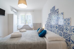 A bedroom with a bed, white towels, a blue patterned wall, and a window with curtains.