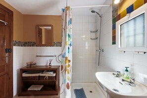A bathroom with a shower, a sink, a mirror, and a wooden cabinet.