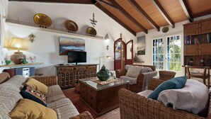 Un salón acogedor con muebles de mimbre, un televisor y objetos decorativos en estanterías.