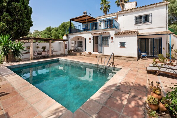 A pool area with a clear blue pool, a covered patio, and a two-story building with balconies.