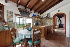Cocina rústica con vigas de madera, una mesa de comedor con sillas y una vista por la ventana.